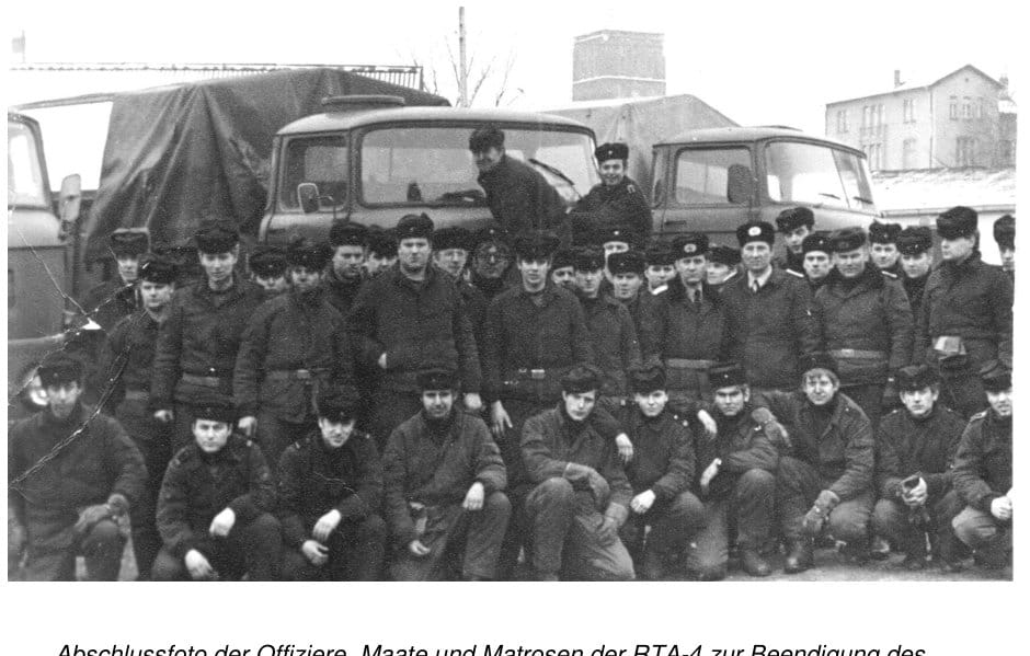 Großes Gruppenfoto von rund fünfzig Marineangehörigen in Winterkleidung mit Pelzmützen vor mehreren LKW, im Hintergrund Werkhallen