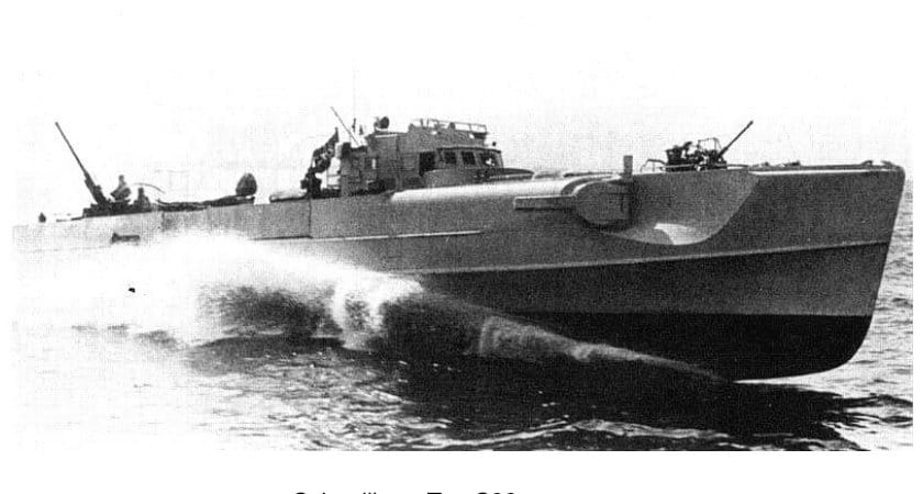Ein Schnellboot läuft mit hoher Fahrt und breiter Heckwelle, an Deck stehen Besatzungsangehörige an den Maschinenkanonen